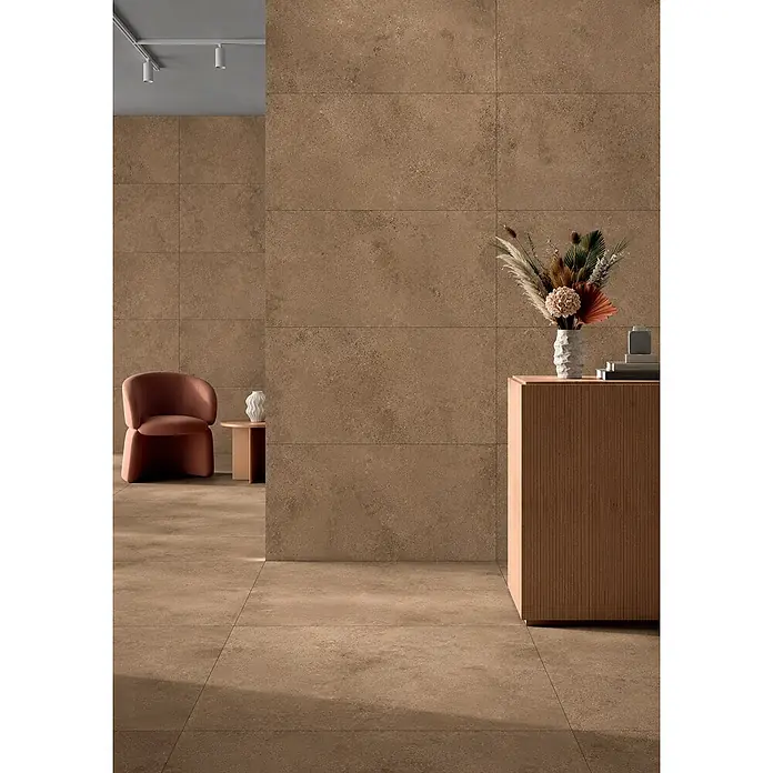 Feinsteinzeug-Bodenfliese strukturierter brauner Betonoptik 60x60 -  - Großformatige braune/beige Fliesen in Steinoptik an Wänden und Boden eines modernen Interieurs mit Stuhl und Schrank.