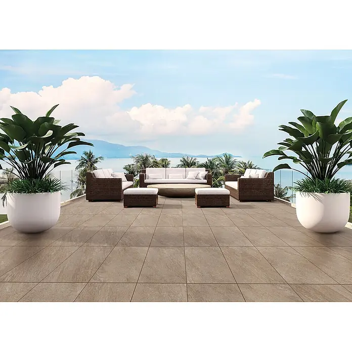 Feinsteinzeug in beiger Steinoptik 60x60, 20 mm, rutschhemmend -  - Beige Outdoor-Fliesen auf einer großzügigen Terrasse mit Loungemöbeln und tropischen Pflanzen, mit Blick auf das Meer und Berge.