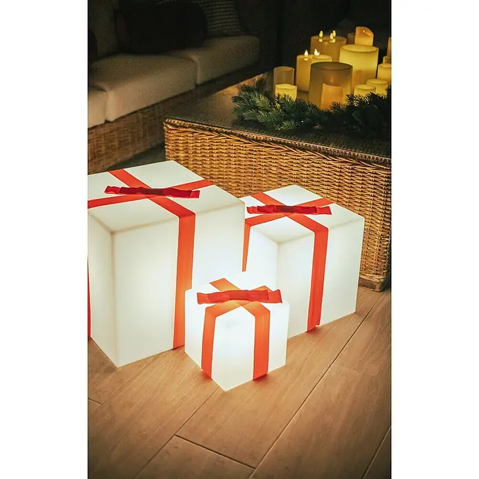 New Garden Figura LED navideña Cubo Gifty 40 Solar - 40 x 40 x 40 cm, Blanco, A batería, LED - Tres cajas de regalo blancas luminosas con cintas rojas sobre suelo de madera en un ambiente acogedor. Luces decorativas navideñas.