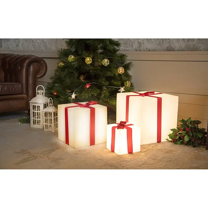 New Garden Figura LED navideña Cubo Gifty 40 Solar - 40 x 40 x 40 cm, Blanco, A batería, LED - Tres cajas de regalo blancas luminosas con cintas rojas, de varios tamaños, decoran una escena navideña festiva bajo un árbol.