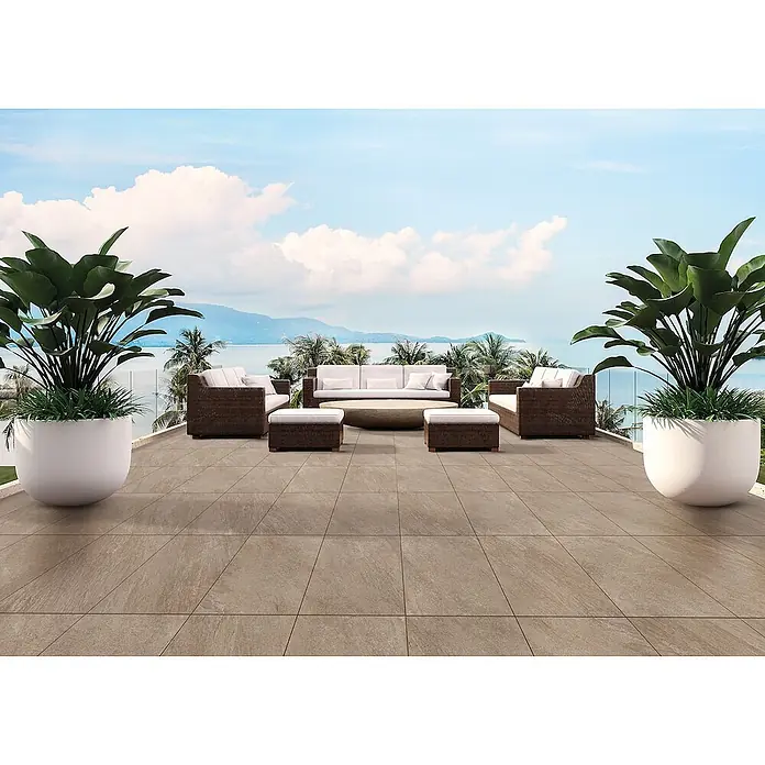 Feinsteinzeug in beiger Steinoptik 60x60, 20 mm, rutschhemmend -  - Große hellbraune Terrassenfliesen auf einer Außenterrasse mit Sitzgelegenheiten und Pflanzen, mit Meerblick.