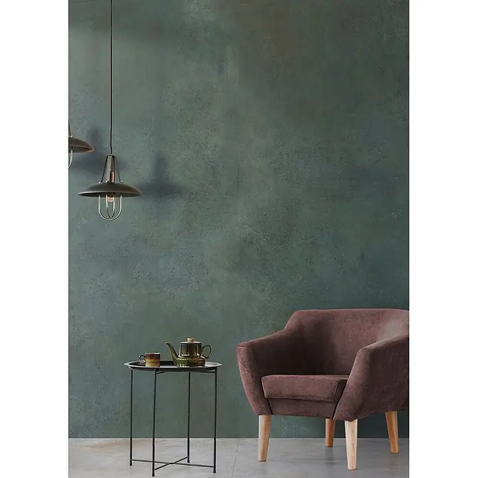 Feinsteinzeug in metallischer grüner Betonoptik 80x80 - Ital. Fliesen -  - Texturierte dunkeltürkise Wand mit Used-Look, akzentuiert eine gemütliche Ecke mit Sessel und Beistelltisch.