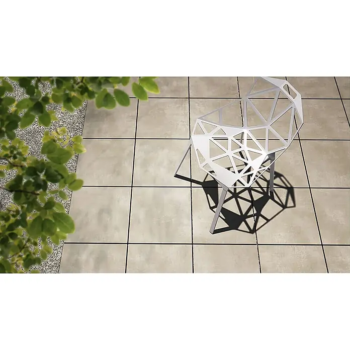 Feinsteinzeug in elfenbeinfarbener Harzoptik 30x60 - Italienische Fliesen -  - Weißer geometrischer Stuhl wirft Schatten auf helle Terrassenfliesen, mit grünem Laub im Eck.