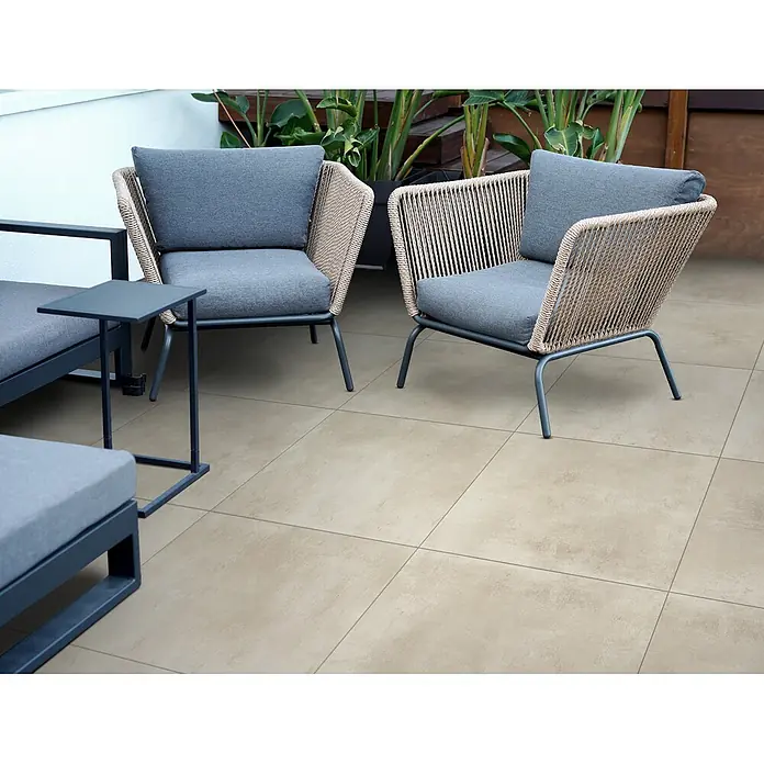 Feinsteinzeug in elfenbeinfarbener Harzoptik 30x60 - Italienische Fliesen -  - Moderne Outdoor-Sessel mit grauen Kissen und geflochtenen Lehnen auf hellen Terrassenfliesen. Ein kleiner Beistelltisch ist dabei.