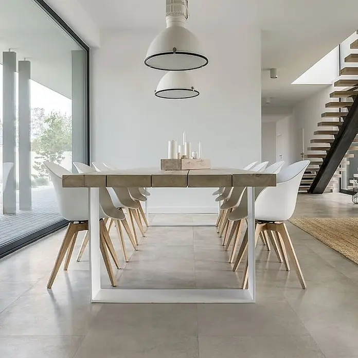 Feinsteinzeug in gewachster elfenbeinfarbener Betonoptik 80x80 -  - Moderner Esstisch mit heller Holzplatte und weißem Metallgestell, umgeben von weißen Stühlen mit Holzbeinen, in einem hellen Esszimmer.