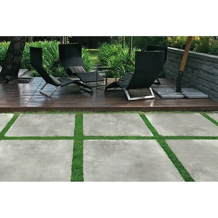 Feinsteinzeug in hellgrauer Harzoptik 60x120, rutschhemmend - Ital. Fliesen -  - Moderne hellgraue Betonplatten mit sattem Gras in den Fugen bilden eine stilvolle Terrasse neben einem Holzdeck.