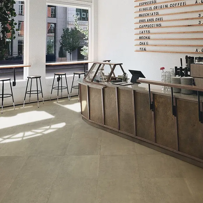 Feinsteinzeug in zeitgenössischer taupefarbener Betonoptik 60x60 -  - Großformatige Feinsteinzeugfliesen in warmem Beige-Grau mit Natursteinoptik auf einem Caféboden.