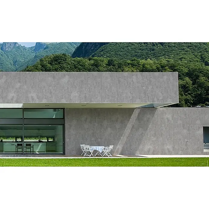 Feinsteinzeug in hellgrauer Harzoptik 30x60 - Italienische Fliesen -  - Moderne Gebäudefassade mit großen grauen Betonoptik-Paneelen, einer großen Glasfront und Außenterrasse, vor grüner Bergkulisse.