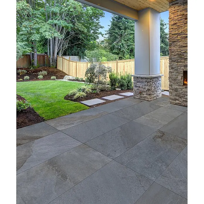Feinsteinzeug in Steinoptik 60x120, 20 mm, rutschhemmend - Ital. Fliesen -  - Dunkelgraue, strukturierte Outdoor-Fliesen bilden eine geräumige Terrasse und Garten-Trittsteine, umgeben von einem üppigen grünen Rasen.