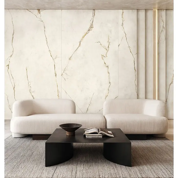 Feinsteinzeug in Gold extra Calacatta-Marmoroptik 60x120 - Ital. Fliesen -  - Modernes Wohnzimmer mit cremefarbenen Modulsofas, dunklem Couchtisch und hellem Teppich vor einer Marmorwand.