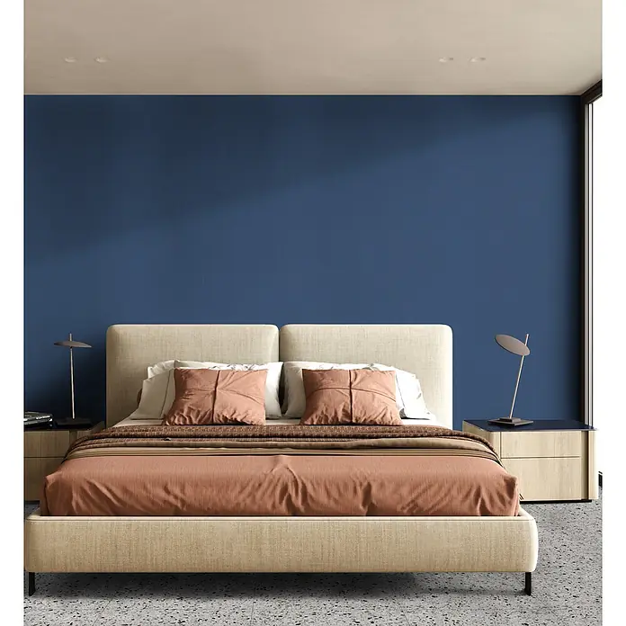 Feinsteinzeug in farbiger dunkelblauer Betonoptik 60x60 - Ital. Fliesen -  - Helles, beigefarbenes Polsterbett mit rotbrauner Bettwäsche, flankiert von Nachttischen vor einer blauen Wand in einem modernen Schlafzimmer.