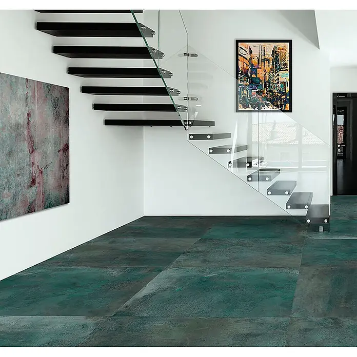 Feinsteinzeug in metallischer grüner Betonoptik 60x120 - Ital. Fliesen -  - Große petrolfarbene Fliesen in Metalloptik, die in einem Raum mit schwebender Treppe eine moderne, industrielle Ästhetik schaffen.