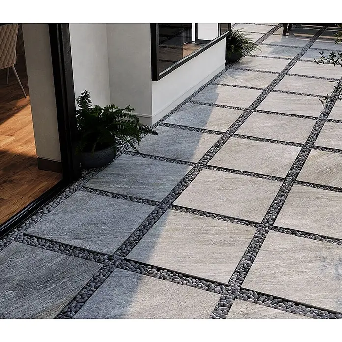 Feinsteinzeug in grauer Steinoptik 60x120, 20 mm, rutschhemmend -  - Helle graue, texturierte Outdoor-Pflastersteine, mit dunklen Kieselsteinen durchsetzt, bilden einen Terrassenweg.
