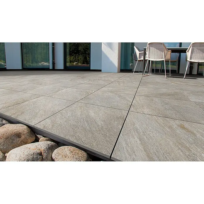 Feinsteinzeug in grauer Steinoptik 60x120, 20 mm, rutschhemmend -  - Großformatige, hellgraue, texturierte Terrassenfliesen, auf einer Terrasse verlegt, mit Möbeln im Hintergrund und Ziersteinen am Rand.