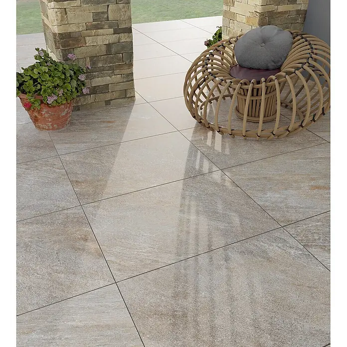 Feinsteinzeug in grauer Steinoptik 60x120, 20 mm, rutschhemmend -  - Helle beige texturierte Terrassenfliesen mit subtilen Variationen, die einen einladenden Außenboden für eine Pflanze und einen Korbstuhl bilden.