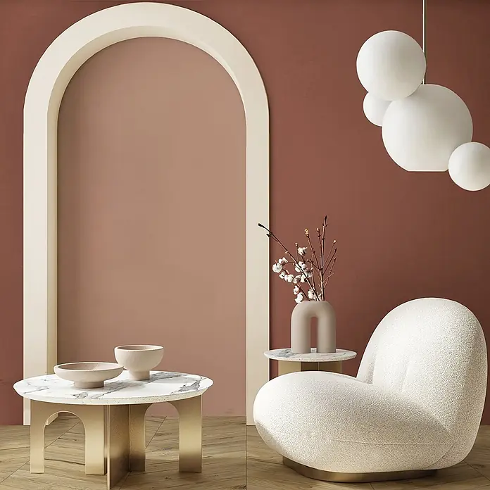 Feinsteinzeug in farbiger roter Betonoptik 60x120 - Italienische Fliesen -  - Ein stilvolles Wohnzimmer mit cremefarbenem Sessel, Marmortischen und dekorativem Bogen. Kugelförmige Pendelleuchten hängen herab.