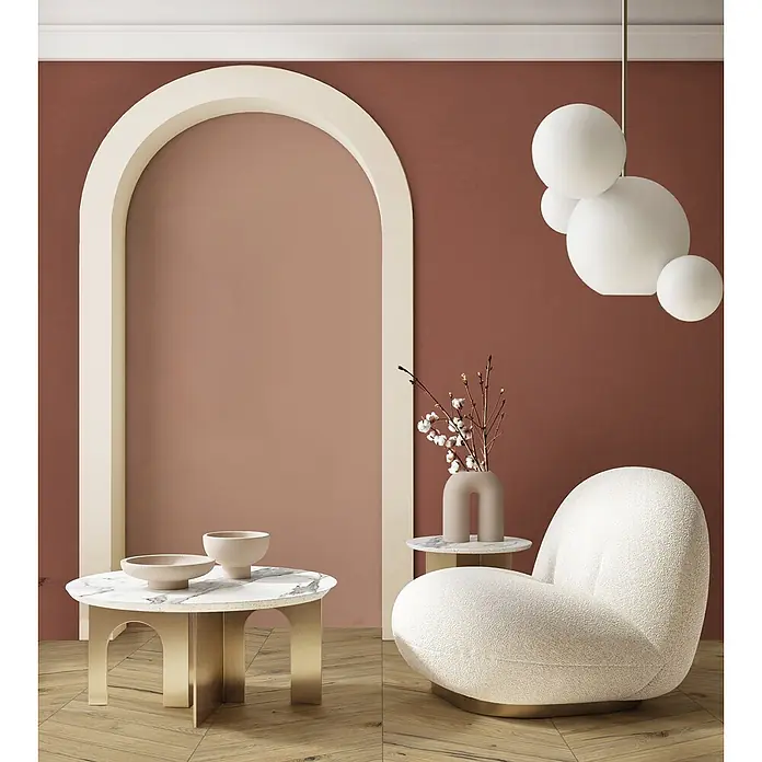 Feinsteinzeug in farbiger roter Betonoptik 60x120 - Italienische Fliesen -  - Gemütliches modernes Wohnzimmer mit cremefarbenem Bouclé-Sessel, rundem Marmor-Couchtisch mit Goldbeinen und kugelförmigen Pendelleuchten vor warmen Wänden.