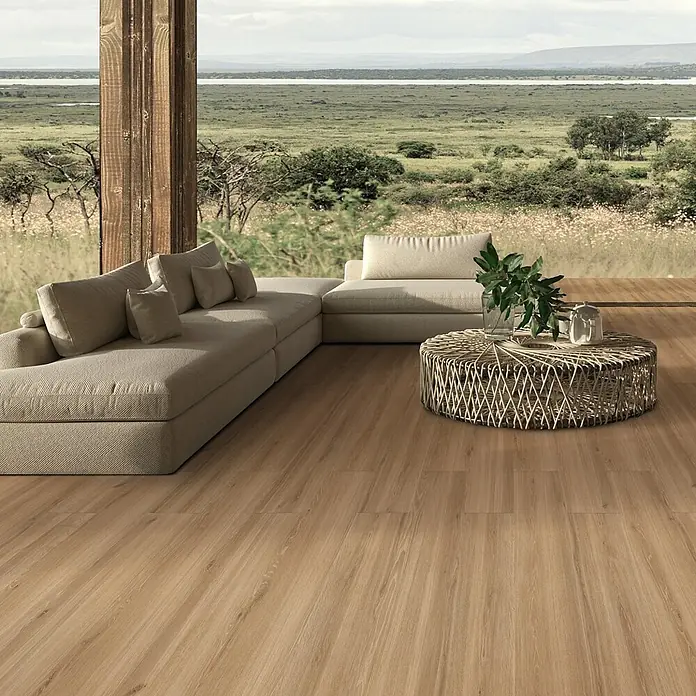 Feinsteinzeug in honigfarbener Holzoptik 20x120, rutschhemmend -  - Helle Holzoptik-Bodenplanken bilden eine warme, natürliche Basis in einem geräumigen Wohnzimmer mit großem Sofa und Aussicht.