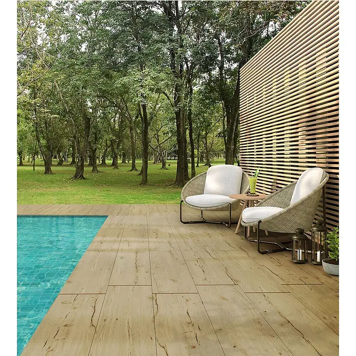 Feinsteinzeug in antiker honigfarbener matter Holzoptik 30x120 -  - Helle Holzoptik-Fliesen bilden eine Poolterrasse mit Gartenstühlen und Bäumen.