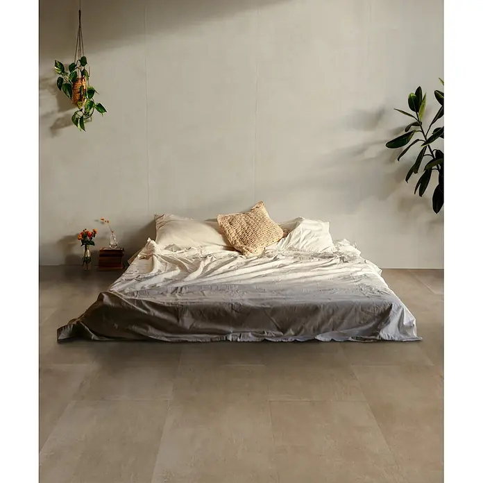 Feinsteinzeug in beiger Harzoptik 80x80 - Italienische Fliesen -  - Niedriges Bett mit heller, zerknitterter Leinenbettwäsche und Textilkissen auf Fliesenboden in minimalistischem Raum.