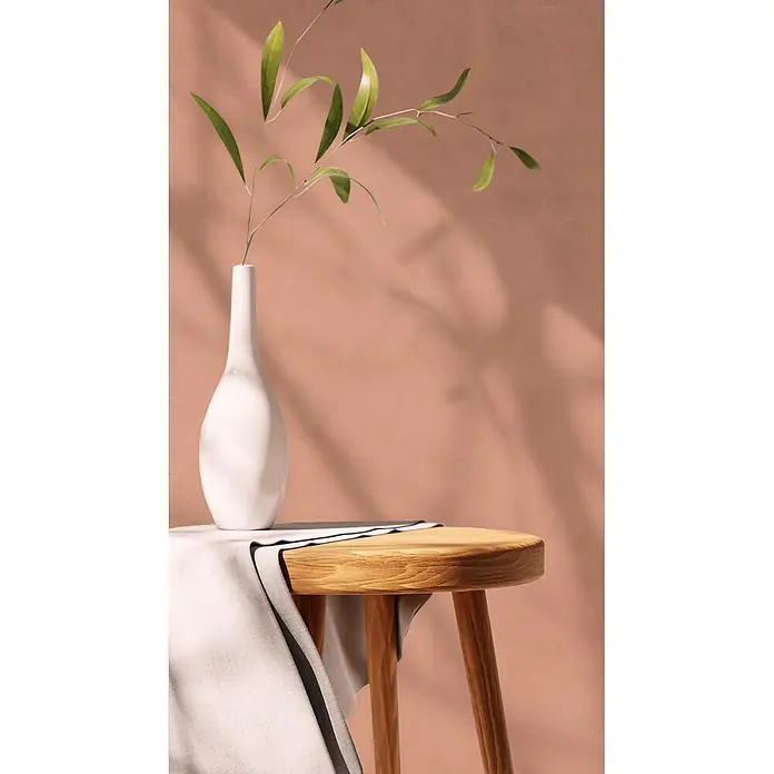 Feinsteinzeug in farbiger rosafarbener Betonoptik 60x120 - Ital. Fliesen -  - Runder Holztisch mit weißer Vase und grünen Blättern, bedeckt mit hellem Stoff.
