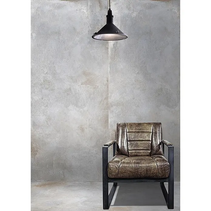 Feinsteinzeug in metallischer hellgrauer Betonoptik 60x120 - Ital. Fliesen -  - Industrielle schwarze Pendelleuchte beleuchtet einen Sessel aus braunem Used-Leder mit dunklem Metallrahmen.