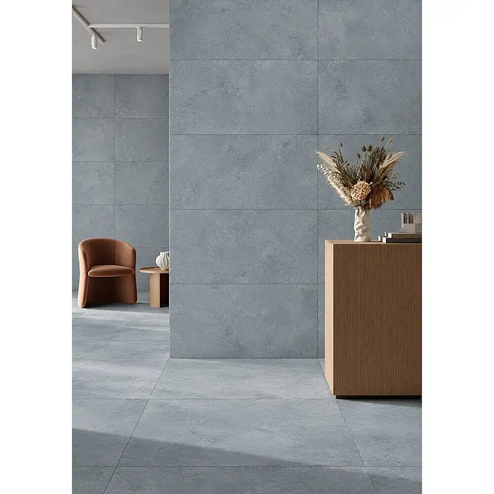 Feinsteinzeug in blauer Betonoptik 120x120 - Italienische Fliesen -  - Großformatige graue Fliesen bedecken Boden und Wände eines modernen Raumes, schaffen einen minimalistischen und kohärenten Raum.