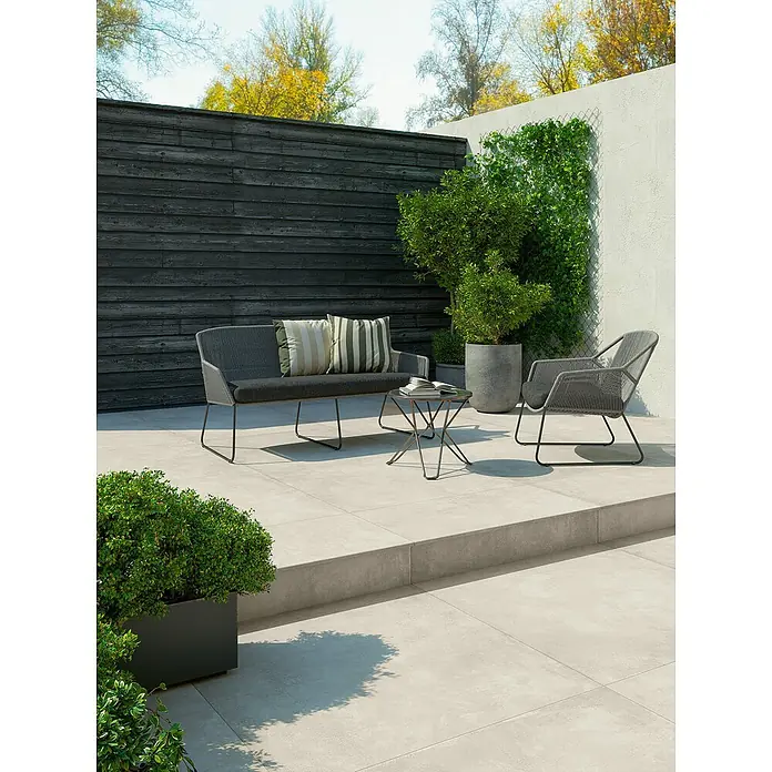 Feinsteinzeug in gewachster weißer Betonoptik 60x120 - Italienische Fliesen -  - Eine moderne Outdoor-Lounge-Sitzgruppe mit dunkelgrauem Sofa, passendem Sessel und Beistelltisch auf einer gefliesten Terrasse.
