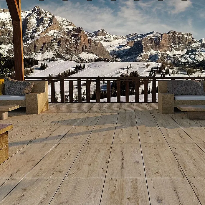 Feinsteinzeug in antiker honig Holzoptik 20x120 - Italienische Fliesen -  - Heller Holzoptik-Bodenbelag auf einer Außenterrasse mit Sitzgelegenheiten, mit Blick auf verschneite Berge.
