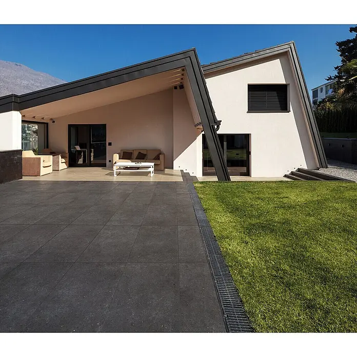 Feinsteinzeug in anthrazit Betonoptik 60x60 - Italienische Fliesen -  - Dunkelgraue Terrassenplatten und lineares Entwässerungssystem am Rasen.