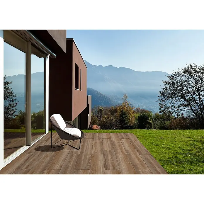 Feinsteinzeug in taupefarbener Holzoptik 20x120 - Italienische Fliesen -  - Holzoptik-Terrassenfliesen auf einer Terrasse vor einem modernen Haus mit Bergblick.