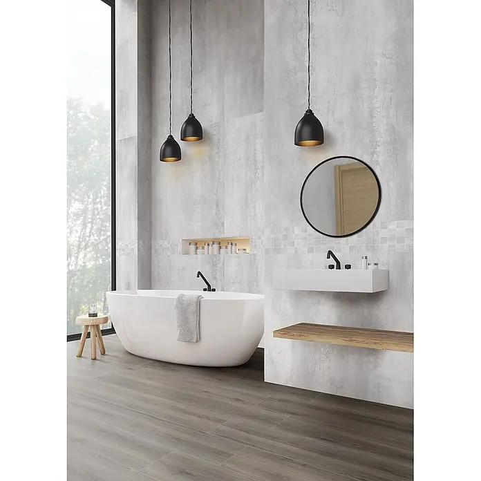 Feinsteinzeug in taupefarbener Holzoptik 20x120 - Italienische Fliesen -  - Modernes Bad mit weißer freistehender Wanne, schwebendem Waschtisch mit Holzablage, rundem Spiegel und schwarzen Pendelleuchten, vor grauen Betonoptikfliesen und Holzoptikboden.