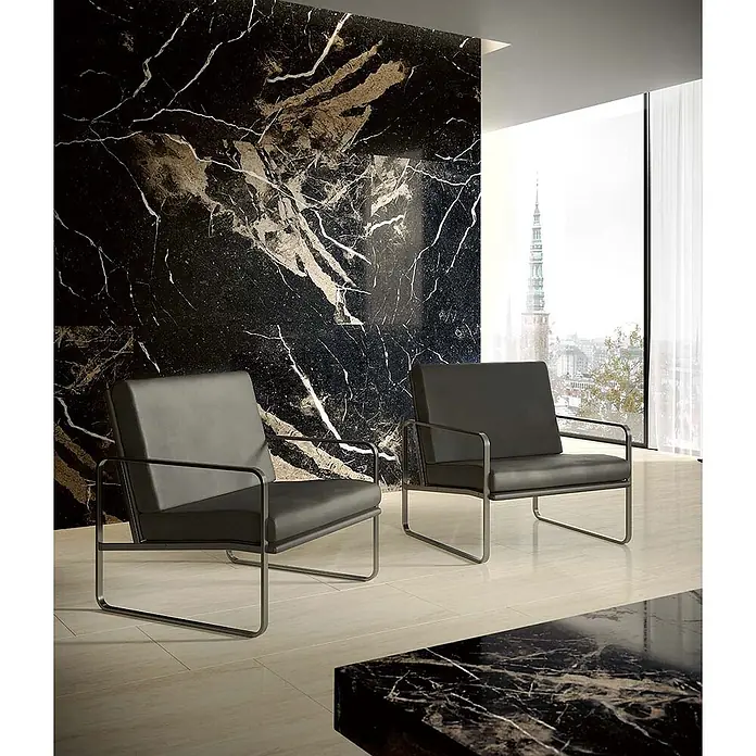 Feinsteinzeug in glänzend beiger Marmoroptik mit schwarzer - Ital. Fliesen -  - Zwei dunkle Sessel mit schlanken Metallrahmen in einem modernen Interieur mit schwarzer Marmorwand.