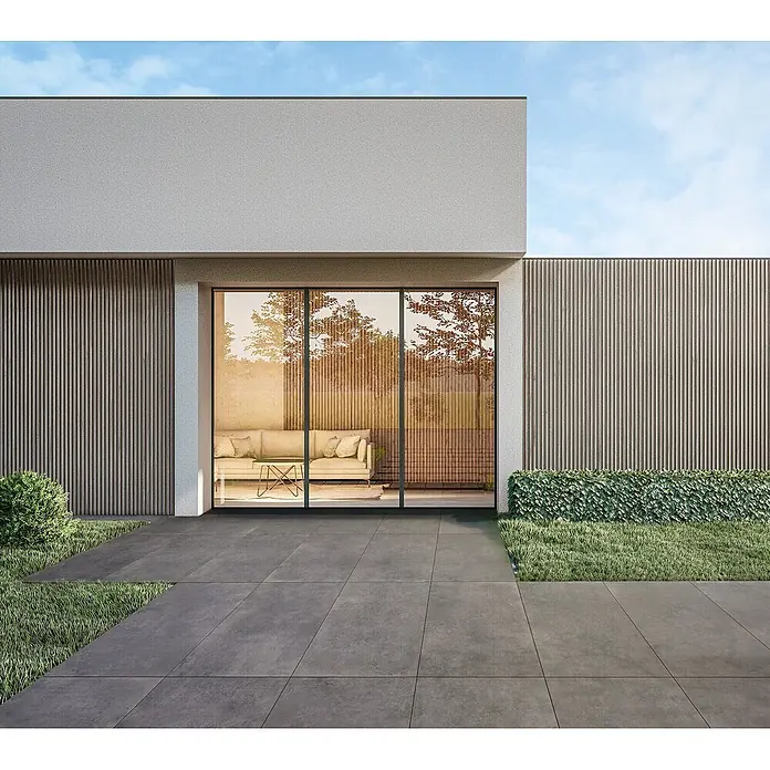 Feinsteinzeug in dunkelgrauer Harzoptik 60x120, rutschhemmend -  - Dunkelgraue Terrassenplatten gestalten einen modernen Außenbereich neben einem Gebäude mit Glasfront und Grünflächen.