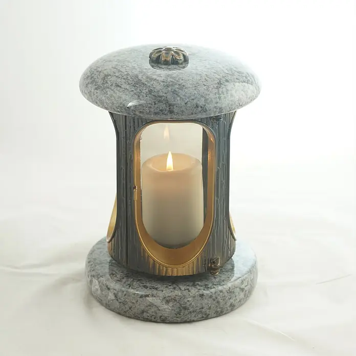 Runde Grablaterne Ø 15 cm, H 22 cm, Granit Orion, Gold-Messing -  - Eine graue gesprenkelte Grablampe aus Stein mit dunklem Metall und goldenen Akzenten, mit einer brennenden weißen Kerze.