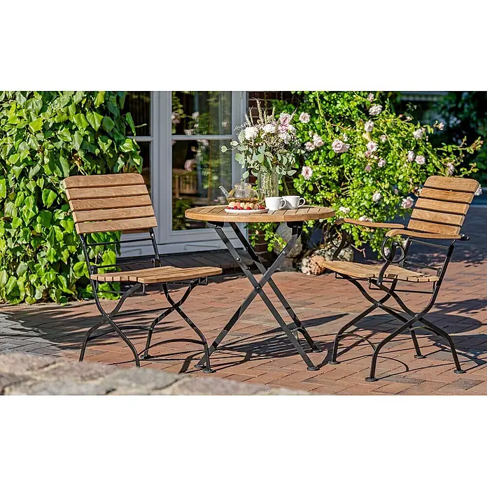 Teak Klapptisch rund 70 cm Massivholz wetterfest für Balkon Terrasse Garten -  - Bistrot-Set aus Holzlatten mit schwarzen Metall-Klapprahmen, auf einer Terrasse mit Grün arrangiert, bereit zum Speisen im Freien.
