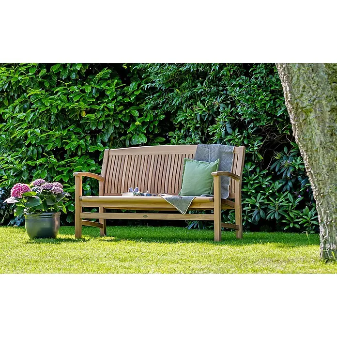 Teak Gartenbank 200 cm Massivholz wetterfest ergonomisch geformt und edel -  - Teakfarbene Holzgartenbank mit grünem Kissen und grauer Decke auf Rasen.