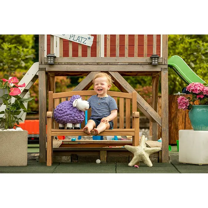 Teak Kinderbank 80 cm Holz Bank unbehandelt massiv wetterfest pflegeleicht -  - Lächelndes Kind sitzt auf Holzbank im Spielplatz mit lila Schaf-Figur.