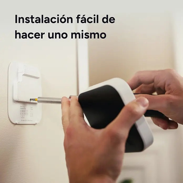 Tado Juego de termostato - Blanco/Negro, Termostáto + Bridge + 2 Cabezales - Manos instalan un dispositivo inteligente blanco en una pared con un destornillador, mostrando una configuración DIY sencilla.