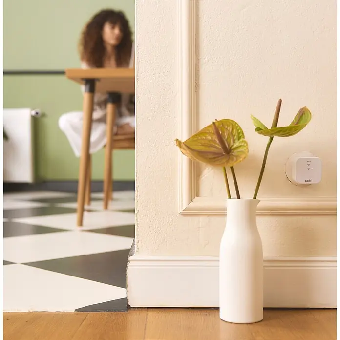 Tado Controlador inteligente Bridge X - Blanco, L x An x Al: 3,1 x 6 x 6 cm - Termostato inteligente tado blanco enchufado a una toma de pared, con luces indicadoras, en un entorno hogareño.