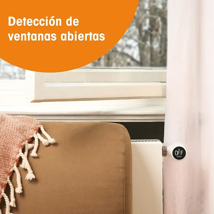 Tado Juego de termostato Bridge X + Cabezal Termoestático X - Blanco, Cabezal y Bridge - Termostato inteligente blanco para radiador, montado en un radiador, muestra 'OFF' y '18.3°', cerca de una ventana.