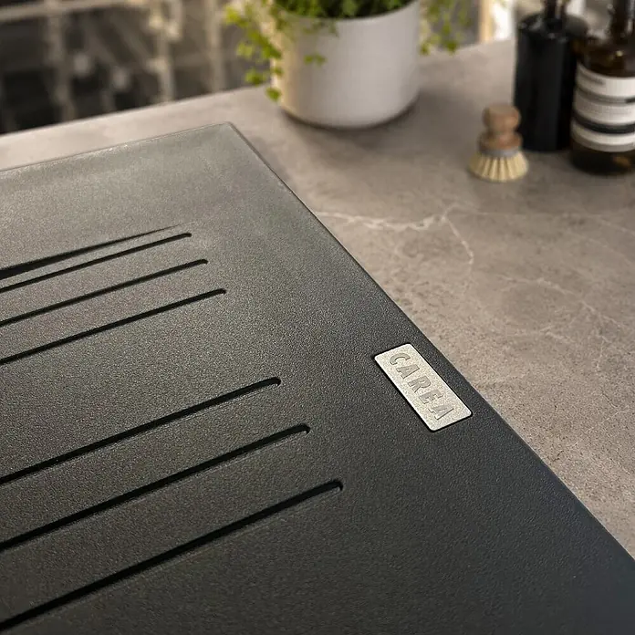 Carea Einbauspüle Muscade - 86 x 50 cm, Schwarz, Hahnloch: Ohne - Dunkelgraues, strukturiertes Abtropfbrett mit parallelen Rillen und einem 'CAREA'-Markenetikett auf einer Küchenarbeitsplatte.