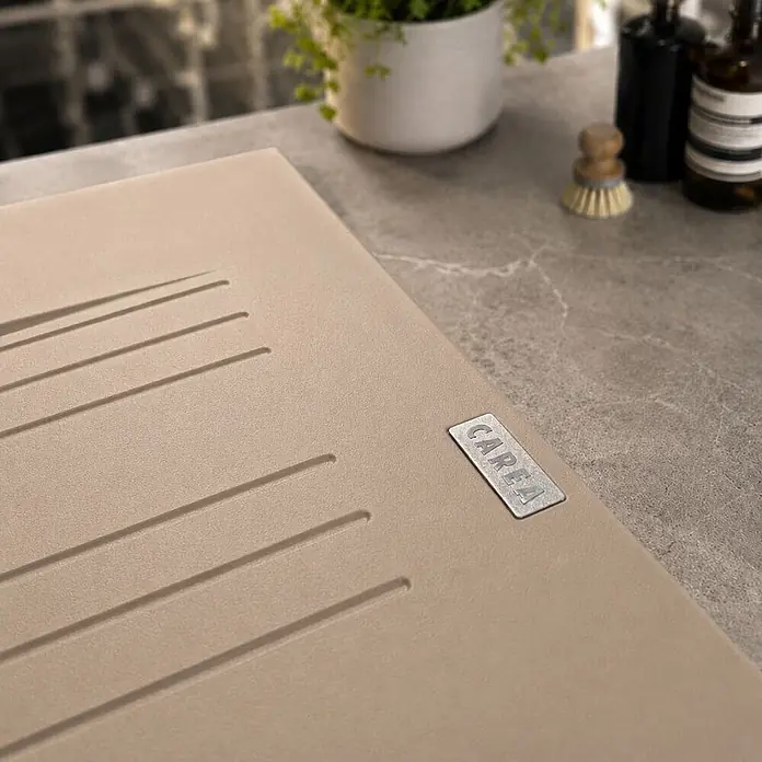 Carea Einbauspüle Muscade - 86 x 50 cm, Taupe - Beige Spülbecken-Abtropffläche mit „CAREA“-Etikett, in gesprenkelte Küchenarbeitsplatte integriert.