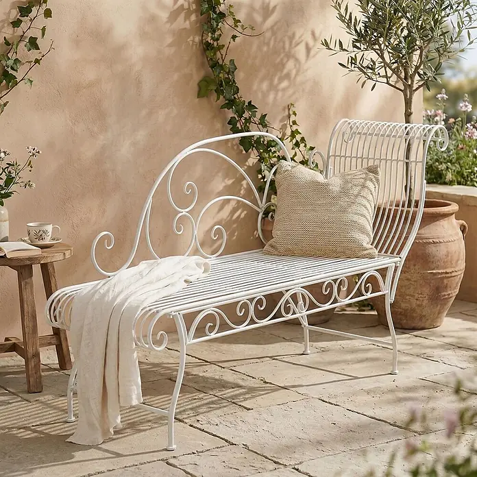 Furnicato Gartenbank Karma Jugendstil aus Eisen -  - Weiße Metall-Gartenliege mit verspielten Schnörkeln, Kissen und Decke, auf sonniger Terrasse platziert.