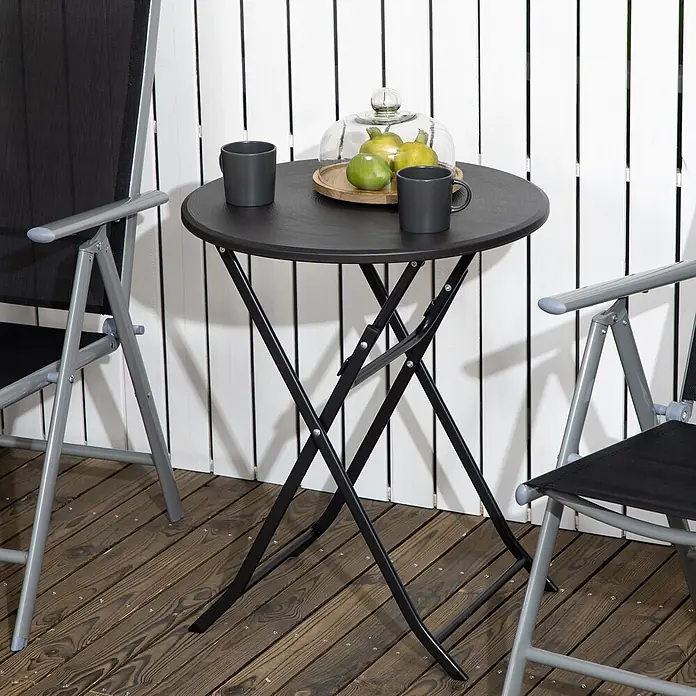 Furnicato Balkontisch klappbar, Ø60 x 73 cm, Dunkelgrau -  - Ein schwarzer runder Klapptisch und zwei dunkelgraue Klappstühle auf einem Holzdeck. Auf dem Tisch stehen zwei Tassen und Obst unter einer Glasglocke.