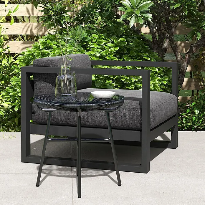 Furnicato Rattan-Beistelltisch schwarz, 50x50x50 cm -  - Dunkelgrauer Outdoor-Sessel mit Kissen und passendem Beistelltisch auf einer Terrasse inmitten üppigen Grüns.