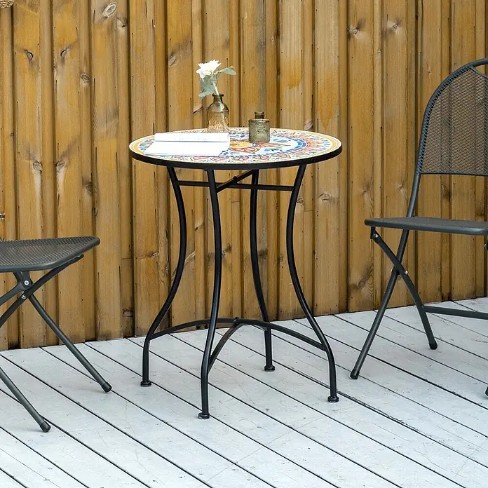 Furnicato Gartentisch Keramik-Mosaik Ø60 x 71 cm -  - Bunter Mosaik-Bistrotisch mit schwarzen Metallbeinen und zwei dunkelgrauen Klappstühlen auf einer Holzterrasse.