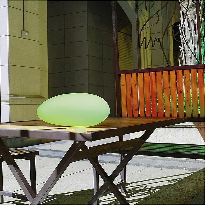 Dekorative Solarleuchte Maki  Steinform -  - Ovale hellgrün leuchtende Lampe auf einem hölzernen Gartentisch.