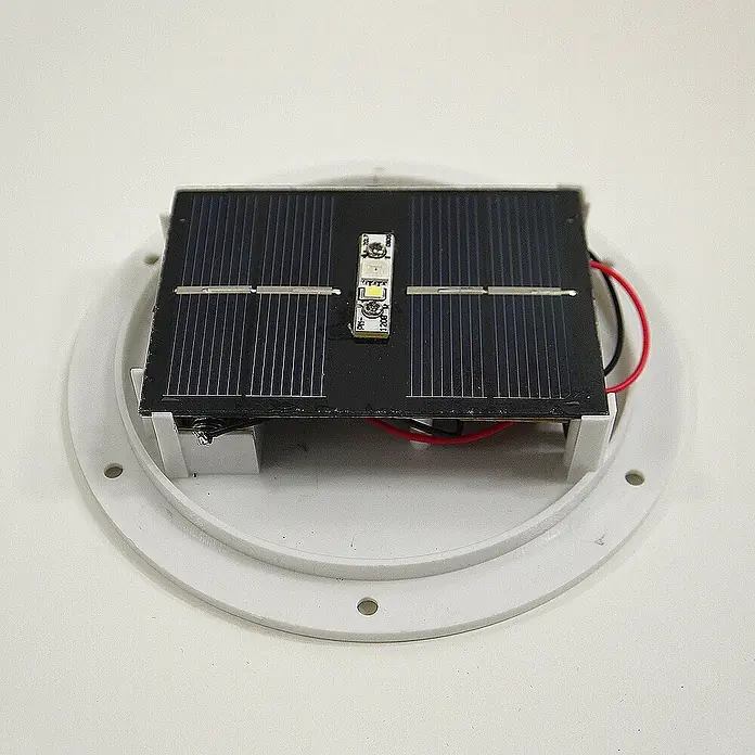 Dekorative Solarleuchte Maki  Steinform -  - Schwarzes Solarpanel mit weißem LED-Streifen auf weißem, rundem Kunststofffuß, Teil einer Solarlampenbaugruppe.