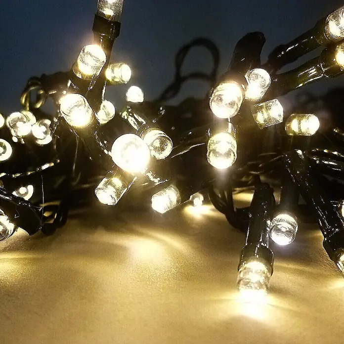 Solarlichterkette 48 LED warmweiß 14,5m -  - Nahaufnahme warmweißer LED-Lichterketten mit dunklen Kabeln, die leuchten und eine weiche Oberfläche erhellen.